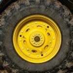 Pneu de trator agrícola com aro amarelo sujo de terra em uma lavoura, ilustrando o desgaste e a importância de saber como escolher e quando trocar os pneus da máquina.
