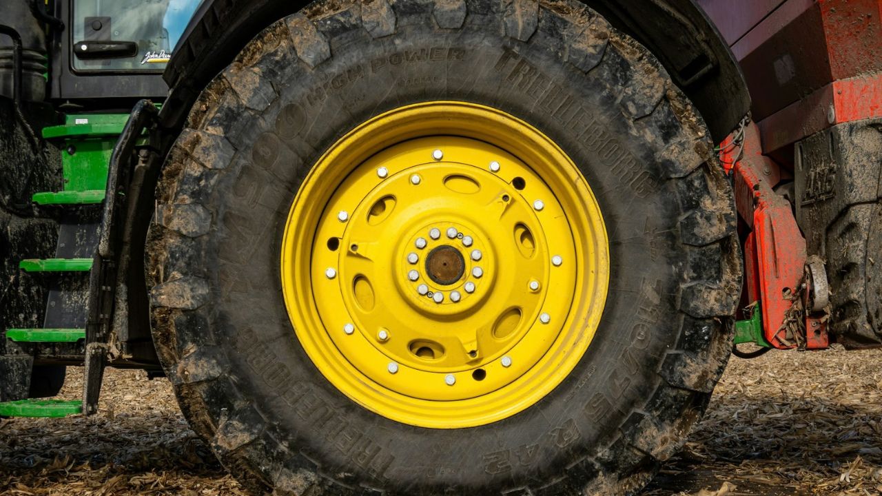 Pneu de trator agrícola com aro amarelo sujo de terra em uma lavoura, ilustrando o desgaste e a importância de saber como escolher e quando trocar os pneus da máquina.